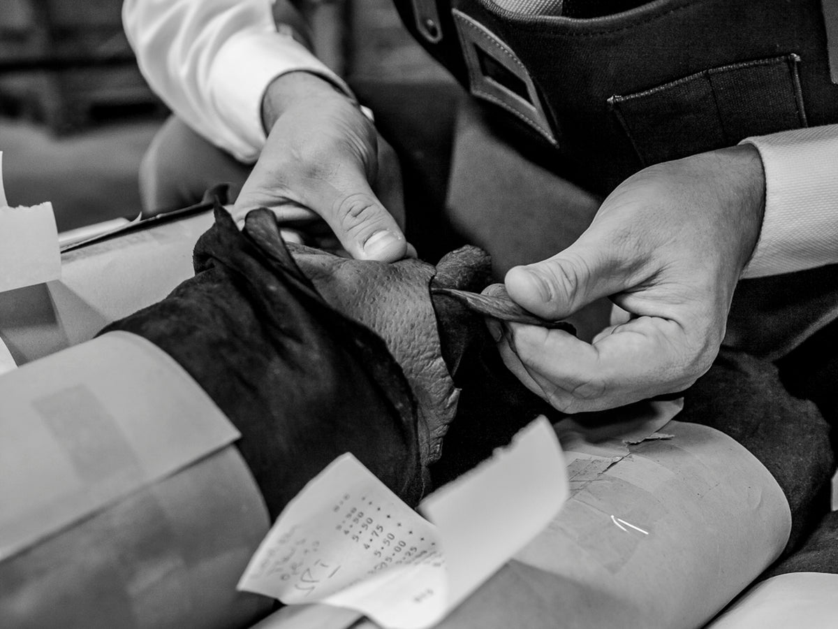 Close-up: hands checking the grain and quality of a raw leather hide in our workshop