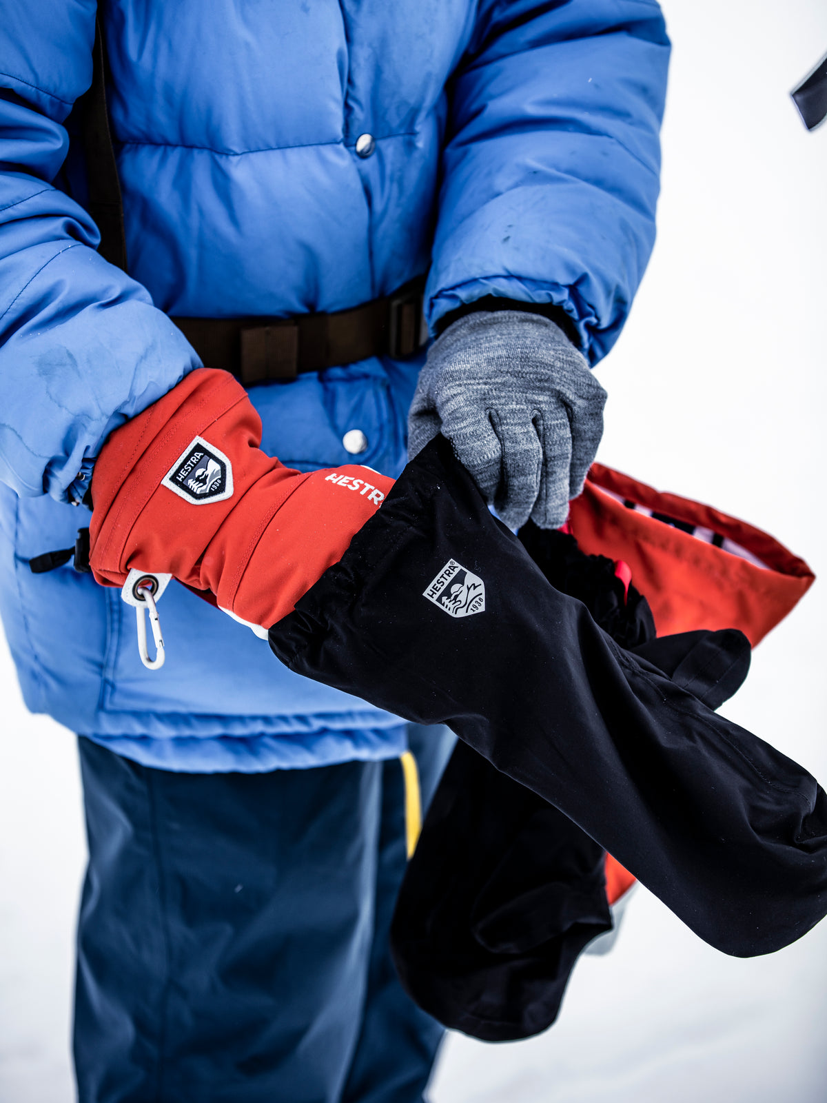 Person in a blue winter jacket showing our layering system, with liner and outer glove